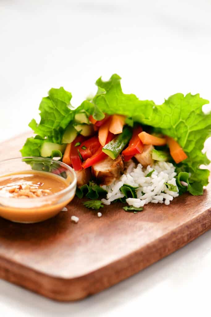 chicken lettuce wrap on a wood board with peanut sauce in a small bowl.