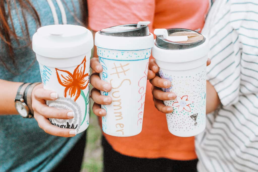 three female hands holding decorated coffee mugs