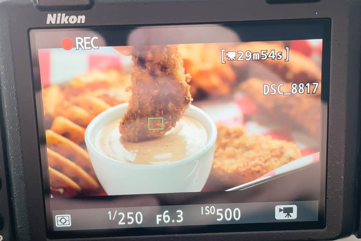 a camera recording a chicken tender being dipping into sauce.