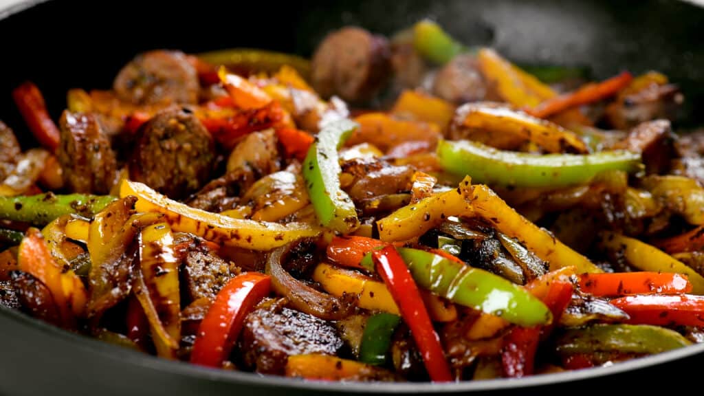 sliced peppers and sausage cooking in a skillet.