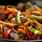 sliced peppers and sausage cooking in a skillet.